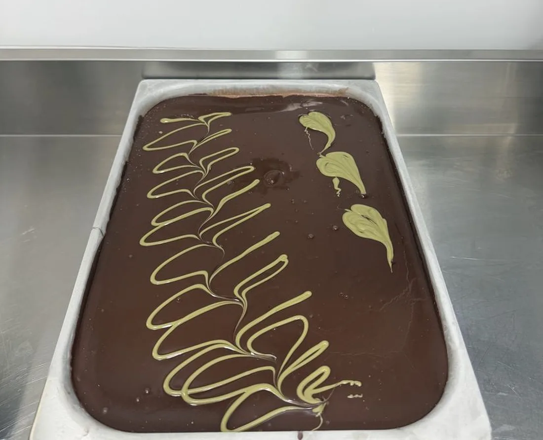 Cubeta de helado de chocolate con veteado de pistacho dibujado a mano sobre encimera de acero